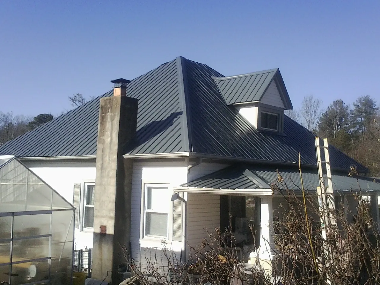 Dark blue standing seam metal roof on a white farmhouse with dormer — Slate & Tile Roof Repair by Roofing Brothers in Moundville