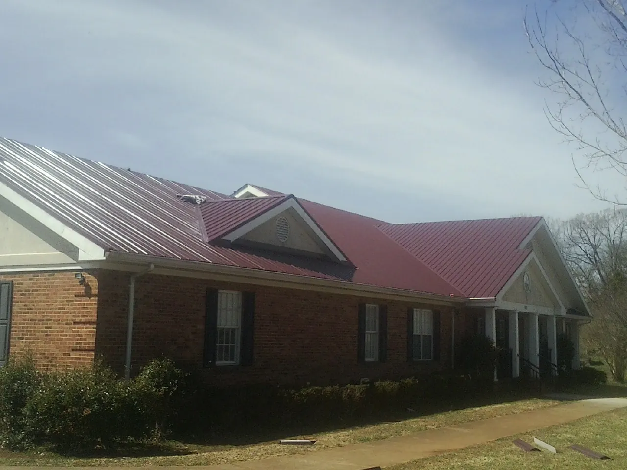 Red metal roof with gabled entries on a long brick building, from a Hail Damage Roof Repair job in Moundville