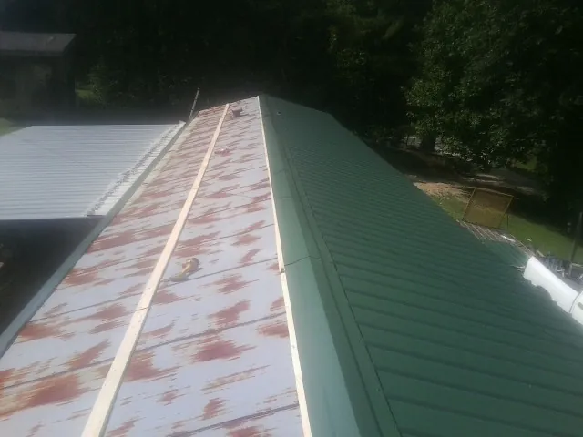 Old rusted panels beside newly installed green metal roofing — Wind Damage Roof Repair by Roofing Brothers in Moundville