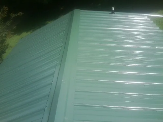 New green metal panels meeting at the ridge of a roof — Flat Roof Repair work by our crew in Moundville