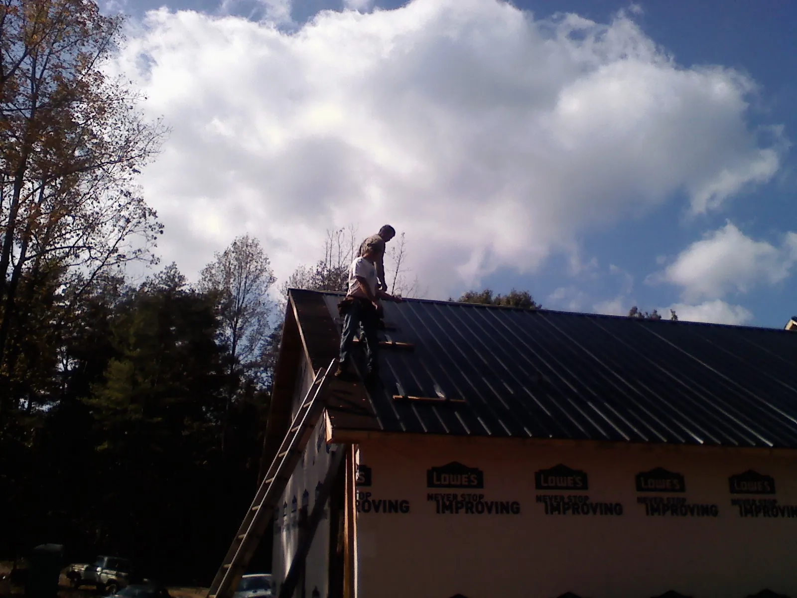 Roofer fastening dark metal panels high against a cloudy sky, from a Roof Inspection job in Moundville