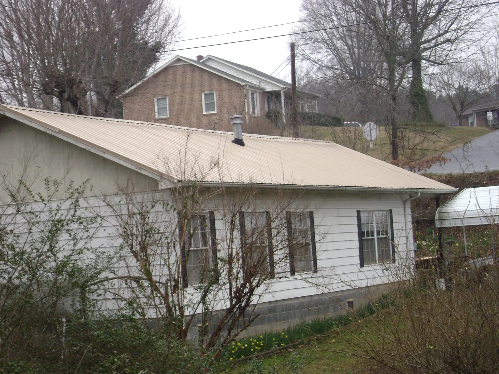 Tan metal roof on a white sided house set into a hillside — Commercial Roofing by Roofing Brothers in Moundville