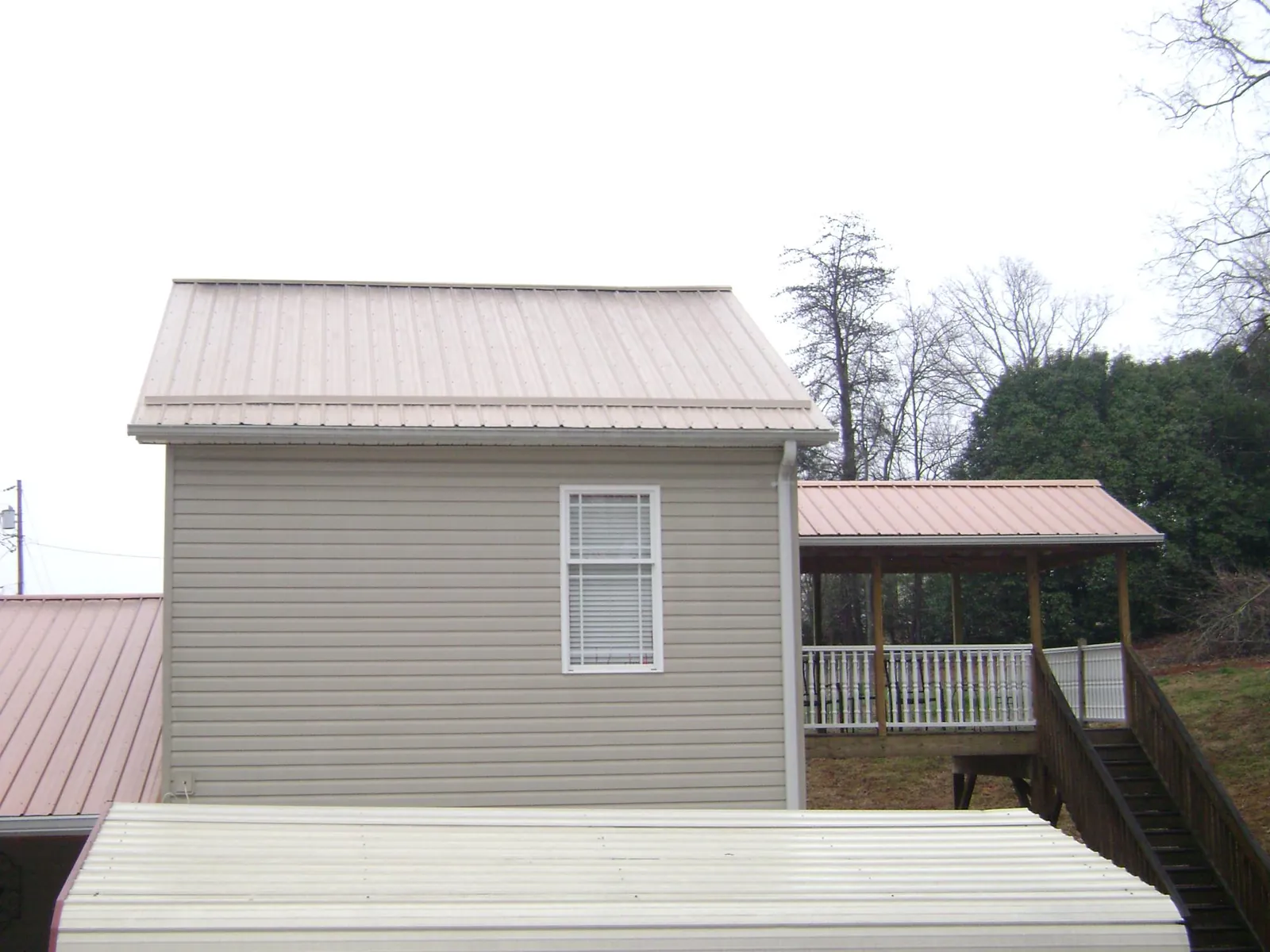 Tan metal roofs on a two story addition and attached porch, from a Roof Replacement job in Moundville